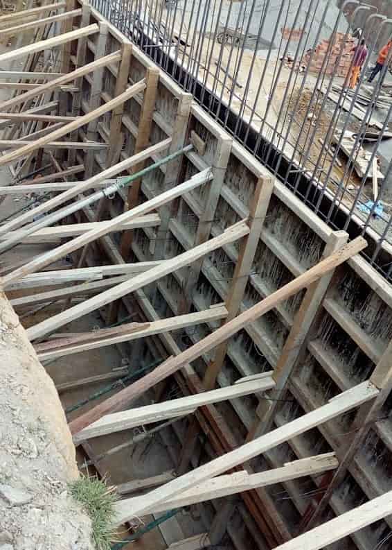 Encofrado de madera y apuntalamiento temporal para un muro de contención o cimentación en la construcción de un centro educativo en Huánuco por arqbimstudio.