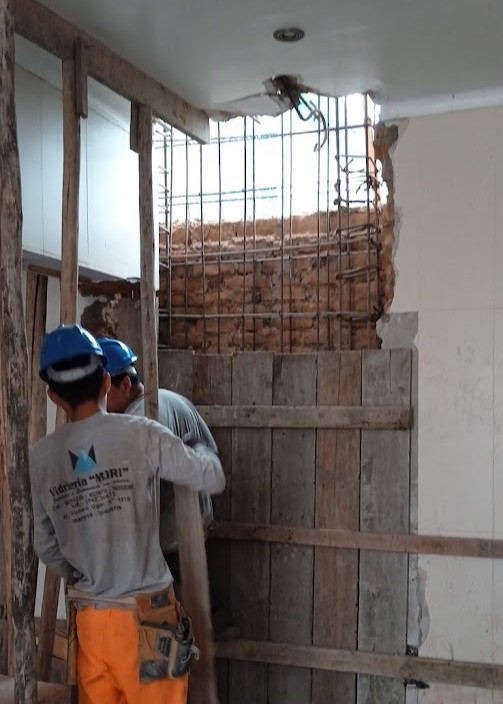 Reforzamiento estructural en casa antigua de Miraflores por ARQBIMStudio, Obreros realizando apuntalamiento de madera y colocación de armadura de acero para muro de ladrillo en remodelación sísmica